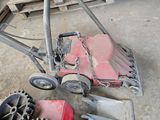 a red lawn mower sitting on the floor next to a pile of wooden pallets