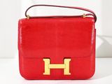 un sac à main rouge orné d'un « H » doré, posé sur une surface blanche