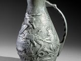 a green vase with a bird on it sitting on a table