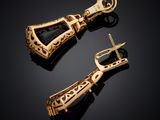 a pair of gold earrings with black stones on a black background