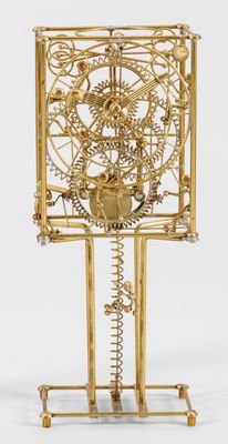 horloge dorée avec des engrenages et des roues, posée sur un socle, sur une surface blanche