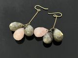 une paire de boucles d'oreilles en pierre rose et verte posées sur un fond noir