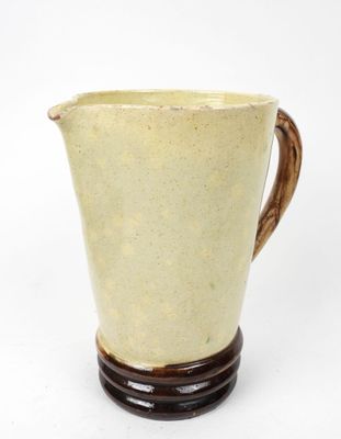 pichet en céramique jaune et marron posé sur un socle en bois, sur fond blanc