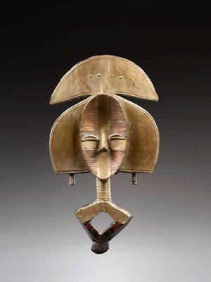 une image représentant un masque en bronze posé sur un socle en bois
