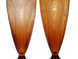 une paire de vases en verre orange posés sur des socles, sur fond blanc