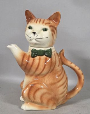 a ceramic cat with a green bow tie and a teapot
