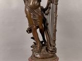 une statue représentant une femme tenant une harpe au sommet d'une horloge