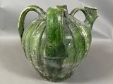 un vase vert orné d'un visage sur fond blanc
