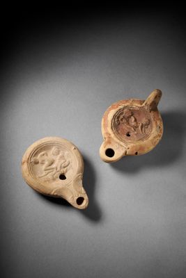 two small clay vessels with faces on them on a gray surface