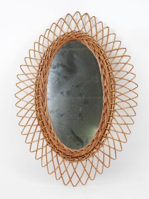 an oval mirror with a wicker frame hanging on a wall