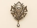 an antique silver broochle with a crystal stone hanging from it ' s center