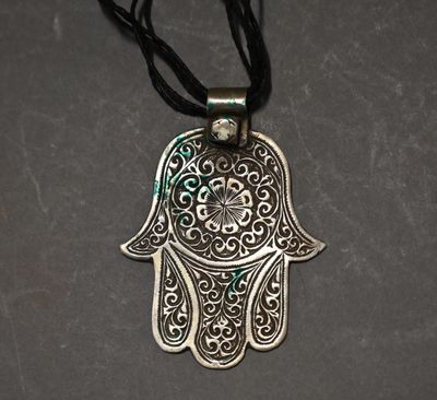 a silver hamsa hand pendant with a black cord on a gray background