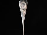 an antique silver spoon with a face on it on a black background
