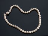 un collier de perles blanches muni d'un fermoir en forme de cœur sur un fond noir