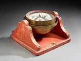 une boussole ancienne en laiton posée sur un socle en bois, elle-même posée sur une surface grise