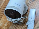 une enceinte blanche posée sur un parquet, à côté d'une télécommande