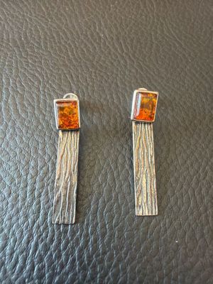 a pair of silver and orange earrings on top of a black leather surface