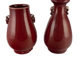 une paire de vases rouges munis d'anses de chaque côté d'un fond blanc
