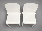 two white plastic chairs sitting next to each other on a gray surface