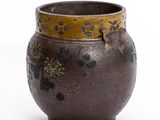 un vase marron orné de fleurs, posé sur un fond blanc