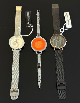 trois montres sont posées sur une surface noire, avec leurs étiquettes encore attachées