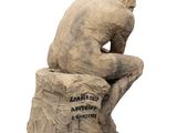statue of a man sitting on top of a rock with a sign on it