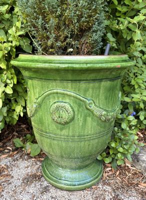 une jardinière verte posée par terre devant un buisson