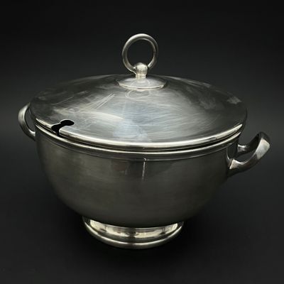 casserole plaquée argent avec couvercle, posée sur un support, sur fond noir
