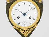 une horloge noire et dorée posée sur un socle, sur fond blanc