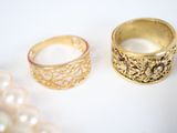 two rings and a pearl necklace on a white surface