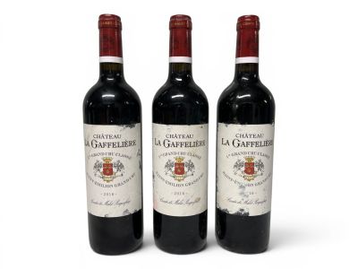 three bottles of red wine sitting next to each other on a white surface