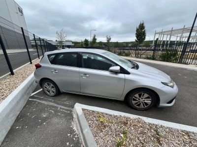 La voiture argentée est garée sur le parking, près de la clôture.