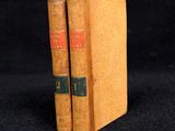 two old books sitting on top of each other on a black surface