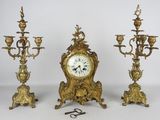 trois bougeoirs dorés et une horloge posés sur une table