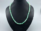 a close up of a necklace with green beads on a mannequin