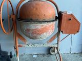 une bétonnière posée contre un mur, avec un godet dessus