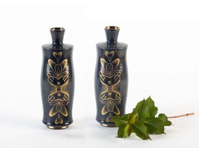 deux vases noirs ornés de motifs dorés, à côté d'une feuille verte