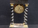 a black and gold clock on a stand on a black background