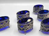 six blue glass bowls with spoons and spoon rest on a white surface