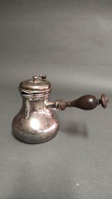 une théière en argent avec une anse en bois posée sur une table