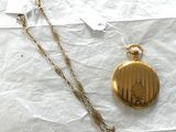 une montre de poche en or et une chaîne en or posées sur un morceau de papier