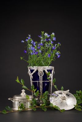 un vase contenant des fleurs bleues, posé à côté d'une théière en argent