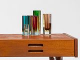 three different colored glass vases sit on a wooden table
