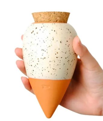 a hand holding a vase with a cork top on it