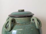 a green vase with a lid sitting on a table