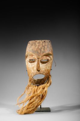 un masque en bois avec de longs cheveux et une barbe, posé sur un socle