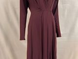 La robe est bordeaux, elle a des manches longues et un col en V.