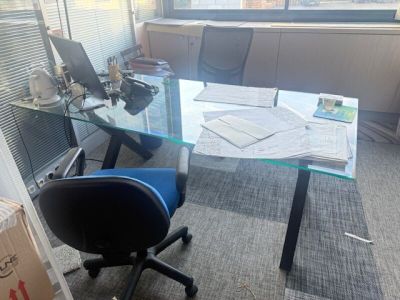 un bureau avec un plateau en verre et une chaise bleue devant une fenêtre