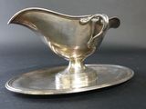a silver gravy on a silver plate on a black table