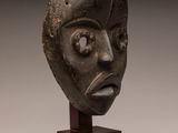 un gros plan sur une sculpture représentant un visage, posée sur un socle en bois
